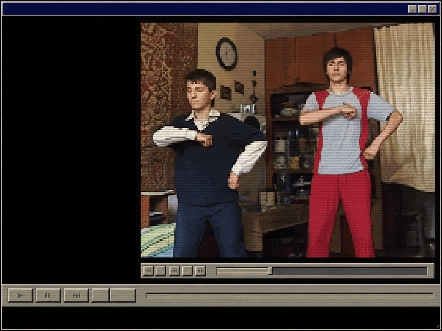 An old media player window: two young men mid-dance in a domestic room with a carpet hung on the wall, a clock and a glass cabinet. One wears a navy sweater over a white shirt, the other a grey shirt with red trousers and suspenders.